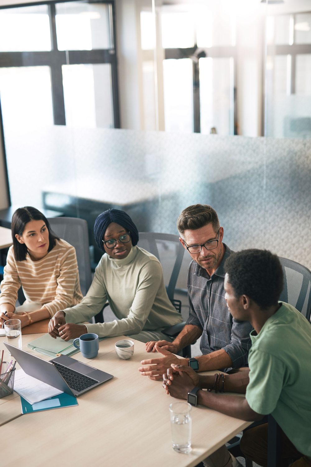 A diverse group of professionals in conversation around a meeting table, representing the partnerships and relationships Ujamii helps build